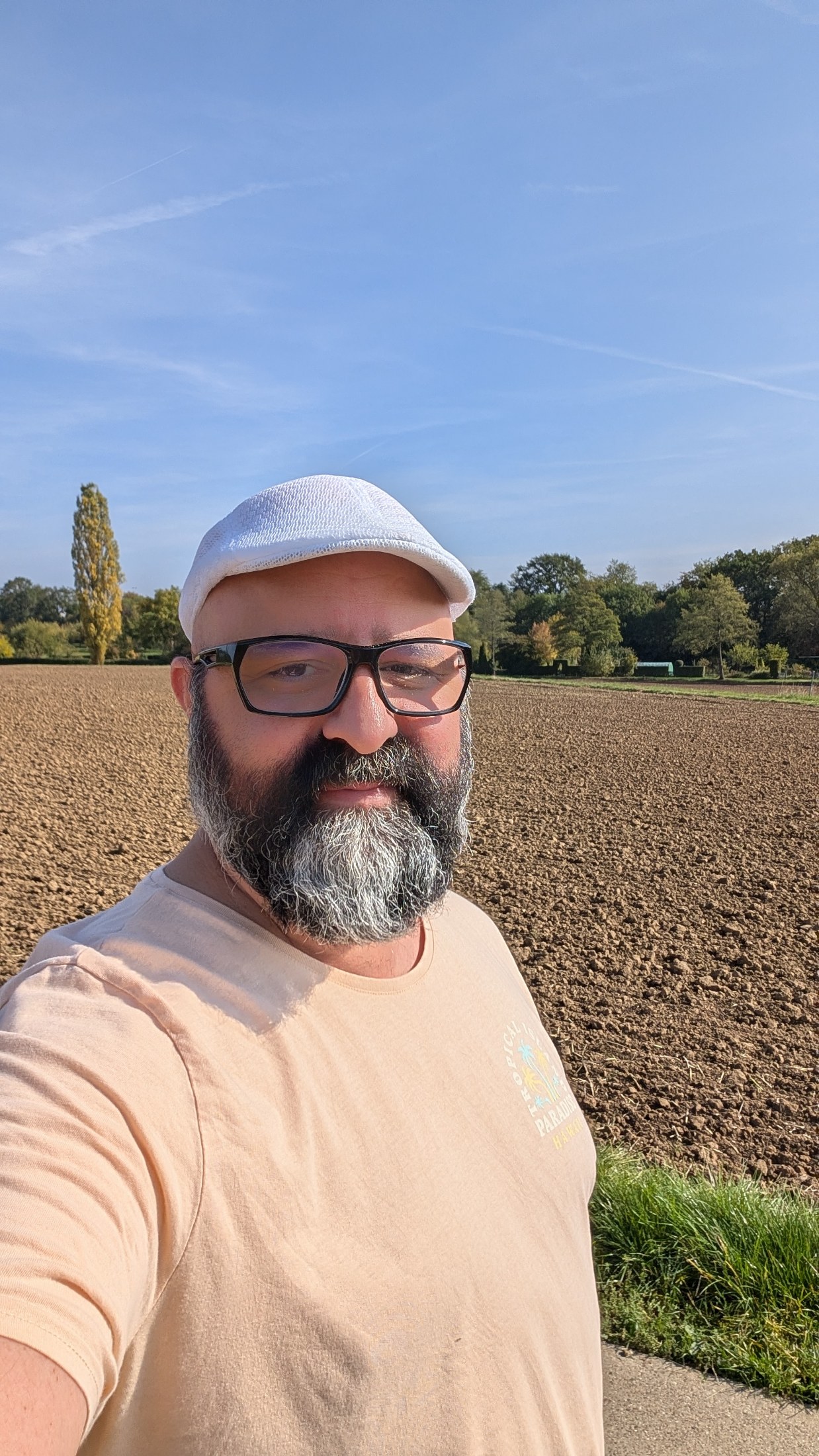 Erol Kücük-Theodosakis steht bei sonnigem Himmel vor einem frisch gepflügten Feld mit Bäumen im Hintergrund